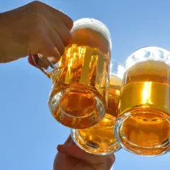 Trzy kufle złotego piwa unoszone na tle błękitnego nieba. Zastanawiasz się, ile kalorii ma piwo?
