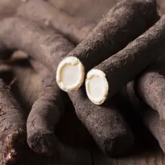 Kilka korzeni skorzonery, zwanej też czarnym korzeniem, leży na drewnianym blacie. Przekrojone końcówki ukazują biały, kremowy miąższ.