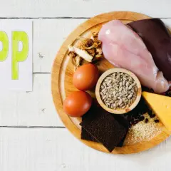 Na talerzu produkty bogate w witaminę PP: wątróbka, pierś kurczaka, jajka, ser, nasiona słonecznika, sezam, fasola, grzyby i chleb.