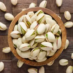 Pistacje w drewnianej misce i rozsypane wokół. Te orzechy to bogactwo białka i błonnika, idealne dla zdrowej diety.