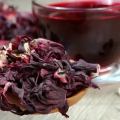 Suszone płatki hibiskusa na drewnianej łyżce i kubek z naparem. Hibiskus co to? To piękny, czerwony napój.