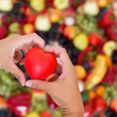Dłonie tworzą serce na tle kolorowych owoców i warzyw. Zastanawiasz się, jakie witaminy na kołatanie serca mogą pomóc?