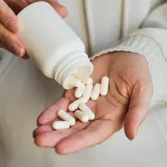 Dłonie wysypują białe kapsułki z butelki na dłoń. To suplement gaba, który może pomóc w relaksacji.