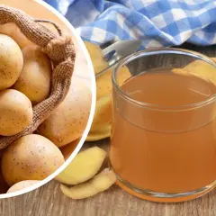 Szklanka z bursztynowym sokiem z ziemniaka obok świeżych bulw i obierków. W tle worek pełen ziemniaków.