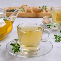 Szklany dzbanek i filiżanki wypełnione aromatyczną herbatą z oregano, ozdobione świeżymi gałązkami.