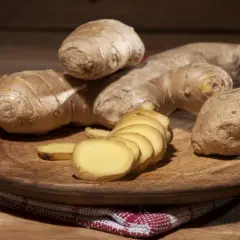 Imbir, znany jako naturalne zioła na cholesterol, prezentowany na drewnianej desce. Kilka korzeni i plasterki świeżego imbiru.