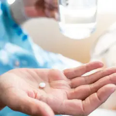 Dłoń trzyma białą tabletkę, przygotowując się do połknięcia. Zrozumienie aspiryna działanie to klucz do ulgi w bólu.