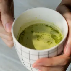 Dłonie trzymają kubek z zieloną herbatą matcha. Warto znać herbata matcha przeciwwskazania przed jej spożyciem.