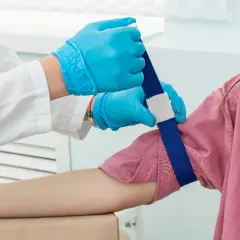 Pobieranie krwi u dziecka z podwyższonymi limfocytami. Ręka dziecka z opaską uciskową, pielęgniarka w rękawiczkach przygotowuje się do wkłucia.