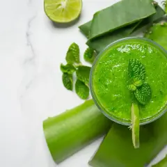 Orzeźwiający, zielony sok z aloesu z miętą i limonką, otoczony świeżymi liśćmi aloesu i kawałkami limonki.