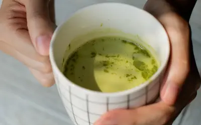Dłonie trzymają kubek z zieloną herbatą matcha. Warto znać herbata matcha przeciwwskazania przed jej spożyciem.