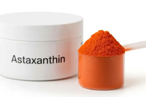 Słoiczek z napisem "Astaxanthin" i miarka wypełniona pomarańczowym proszkiem. Poznaj astaksantyna właściwości!