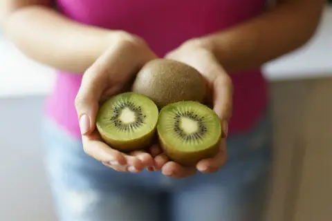 Dłonie trzymają całe i przekrojone kiwi. Czy kiwi jest zdrowe? Tak, to pyszny owoc pełen witamin!