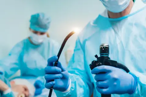 Lekarz w niebieskiej masce i fartuchu przygotowuje endoskop do badania, które może pomóc w diagnostyce przełyku Barretta.
