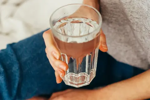 Szklanka wody, idealna na kaca. Dłoń trzymająca chłodny napój, by poczuć się lepiej.