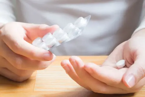 Dłoń trzyma tabletkę, a druga ręka blister. Czy to początek problemów z taurynian magnezu skutki uboczne?