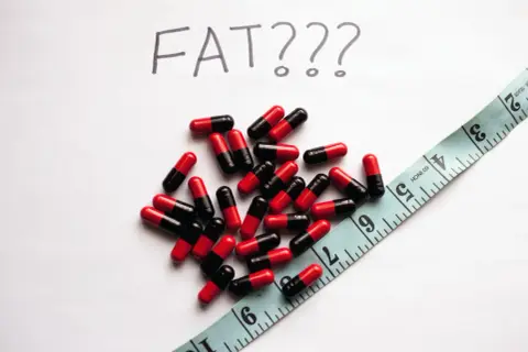 Kapsułki i miarka, a nad nimi napis "FAT???". Czy johimbina co to pomoże zrzucić zbędne kilogramy?
