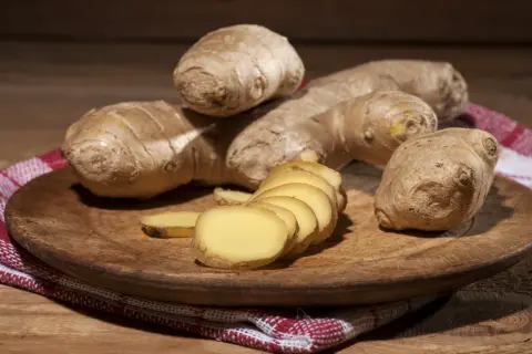 Imbir, znany jako naturalne zioła na cholesterol, prezentowany na drewnianej desce. Kilka korzeni i plasterki świeżego imbiru.