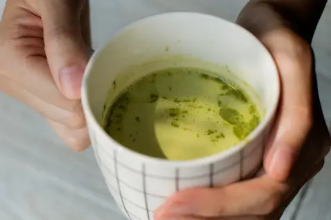 Dłonie trzymają kubek z zieloną herbatą matcha. Warto znać herbata matcha przeciwwskazania przed jej spożyciem.