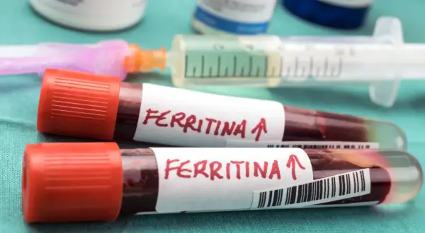Dwie probówki z krwią oznaczone "Ferritina" i strzałką w górę, sugerujące potrzebę podniesienia poziomu ferrytyny. W tle strzykawka i inne materiały medyczne.