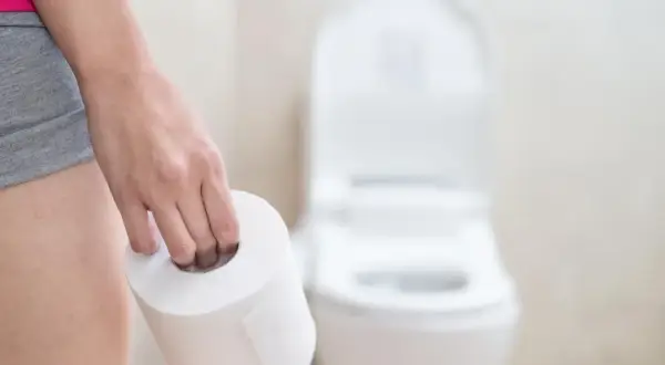 Dłoń trzymająca rolkę papieru toaletowego przed toaletą. Może to sugerować problemy z wypróżnianiem, co powoduje zaparcia.