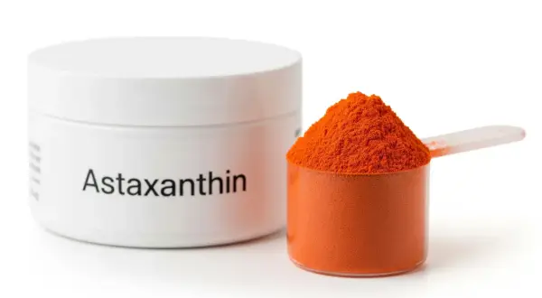Słoiczek z napisem "Astaxanthin" i miarka wypełniona pomarańczowym proszkiem. Poznaj astaksantyna właściwości!