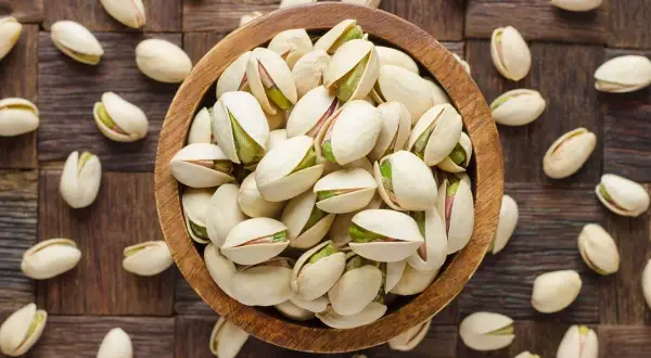 Pistacje w drewnianej misce i rozsypane wokół. Te orzechy to bogactwo białka i błonnika, idealne dla zdrowej diety.