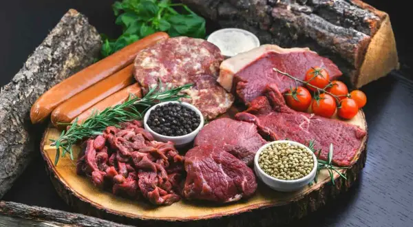 Mięsne bogactwo na drewnianej desce: steki, kiełbaski, mielone, pomidorki i przyprawy. Idealne składniki dla diety carnivore.