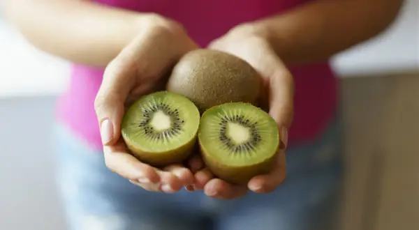 Dłonie trzymają całe i przekrojone kiwi. Czy kiwi jest zdrowe? Tak, to pyszny owoc pełen witamin!