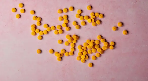 Żółte tabletki na różowym tle. Pamiętaj, z czym nie łączyć magnezu, by uniknąć interakcji.