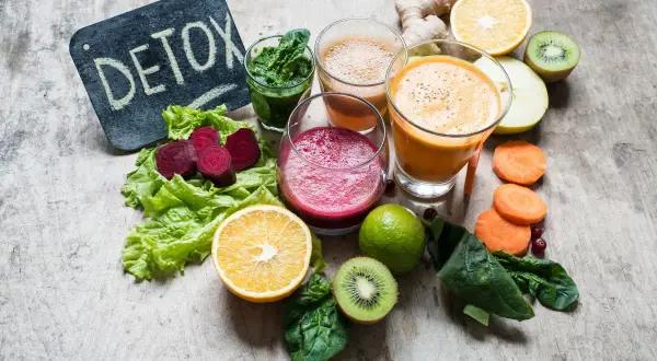 Kolorowe soki i warzywa na drewnianym tle. Tabliczka z napisem "DETOX" sugeruje, że te składniki pomagają w walce z tym, co zakwasza organizm.