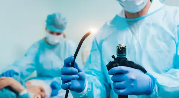 Lekarz w niebieskiej masce i fartuchu przygotowuje endoskop do badania, które może pomóc w diagnostyce przełyku Barretta.