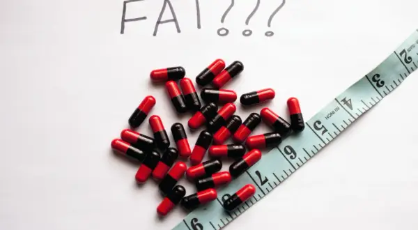Kapsułki i miarka, a nad nimi napis "FAT???". Czy johimbina co to pomoże zrzucić zbędne kilogramy?