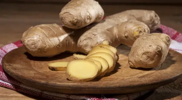Imbir, znany jako naturalne zioła na cholesterol, prezentowany na drewnianej desce. Kilka korzeni i plasterki świeżego imbiru.