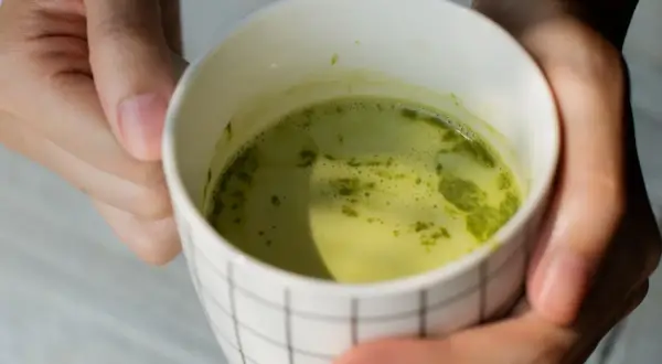 Dłonie trzymają kubek z zieloną herbatą matcha. Warto znać herbata matcha przeciwwskazania przed jej spożyciem.