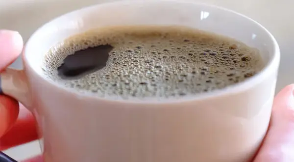 Gorąca kawa w kubku, która pobudza, bo tak działa kofeina. Piana na powierzchni świadczy o świeżości napoju.