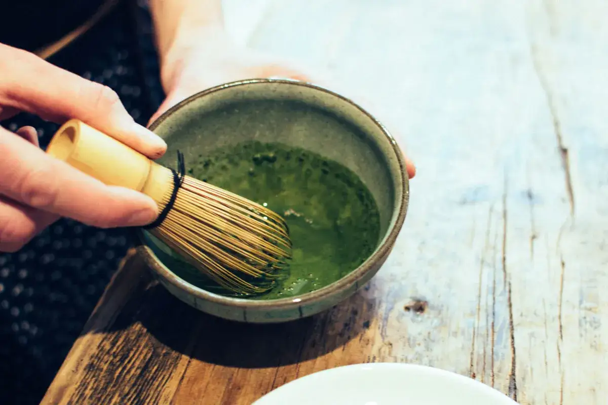 Ręce ubijają zieloną herbatę matcha bambusową miotełką. Warto znać herbata matcha przeciwwskazania przed jej spożyciem.