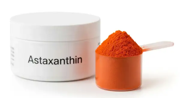Słoiczek z napisem "Astaxanthin" i miarka wypełniona pomarańczowym proszkiem. Poznaj astaksantyna właściwości!