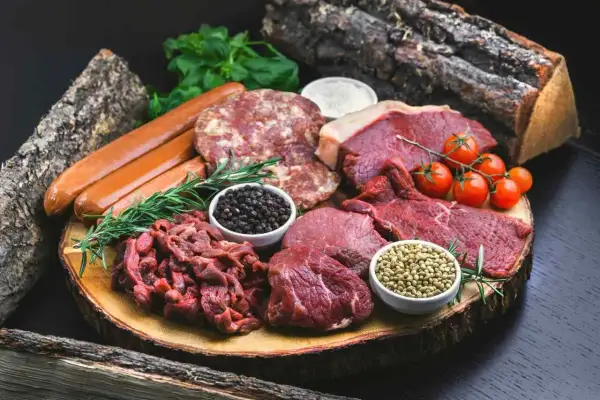 Mięsne bogactwo na drewnianej desce: steki, kiełbaski, mielone, pomidorki i przyprawy. Idealne składniki dla diety carnivore.