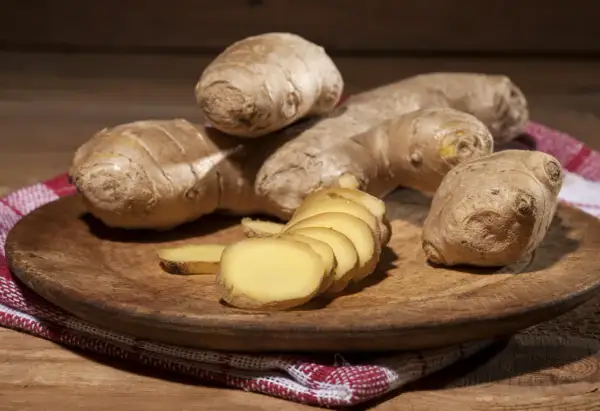 Imbir, znany jako naturalne zioła na cholesterol, prezentowany na drewnianej desce. Kilka korzeni i plasterki świeżego imbiru.